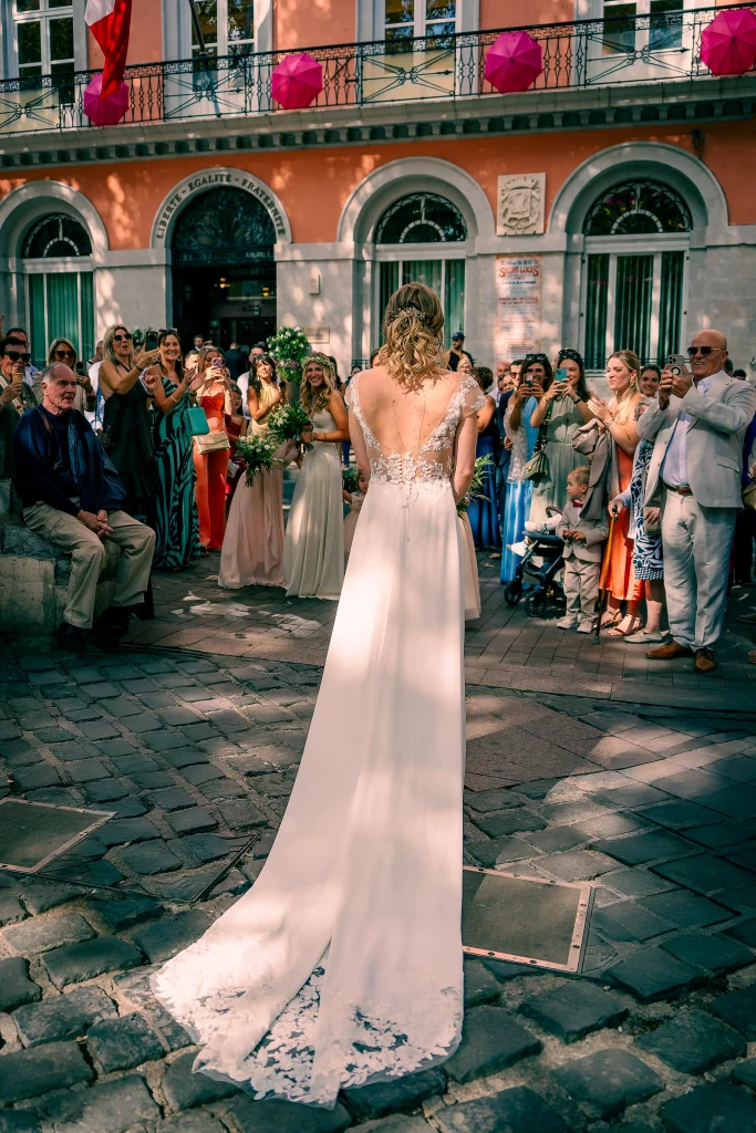 La mariée vue de dos devant la façade d’un bâtiment